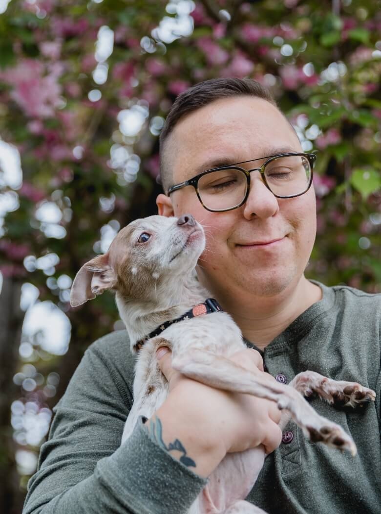 Mann mit Brille hält einen kleinen Hund und lächelt, während er die Augen geschlossen hat