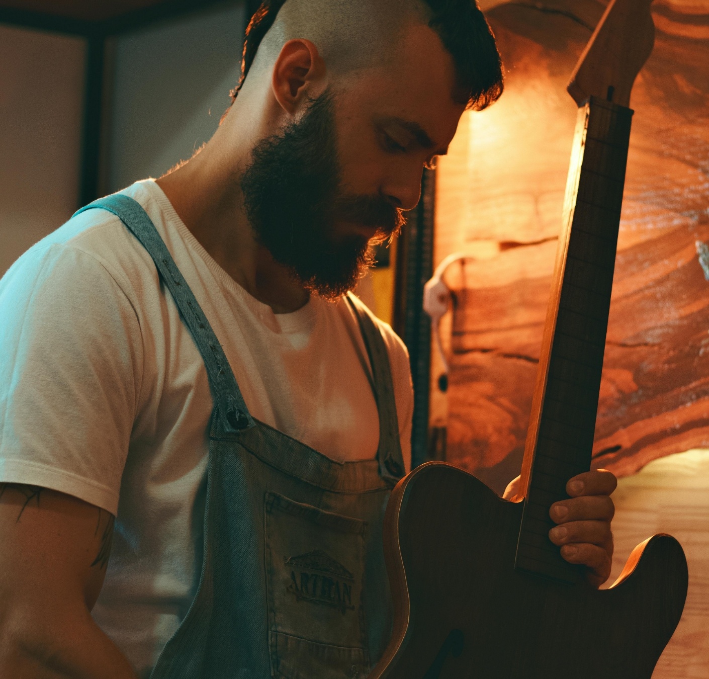 Ein Mann mit Bart und Mohawk-Frisur arbeitet an einer Gitarre in einer Werkstatt.
